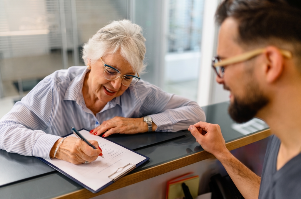 Paciente mayor rellenando un formulario en la recepción de una clínica antes de su cita médica