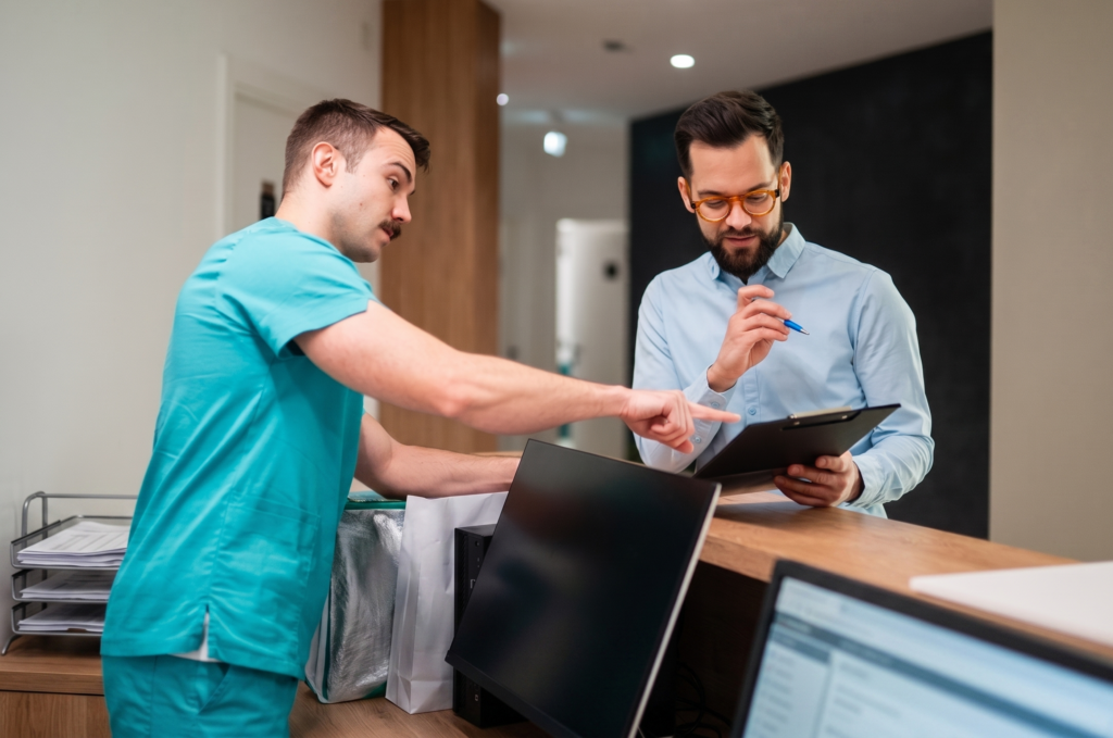 Profesional sanitario atendiendo a un paciente en la recepción de una clínica y revisando información